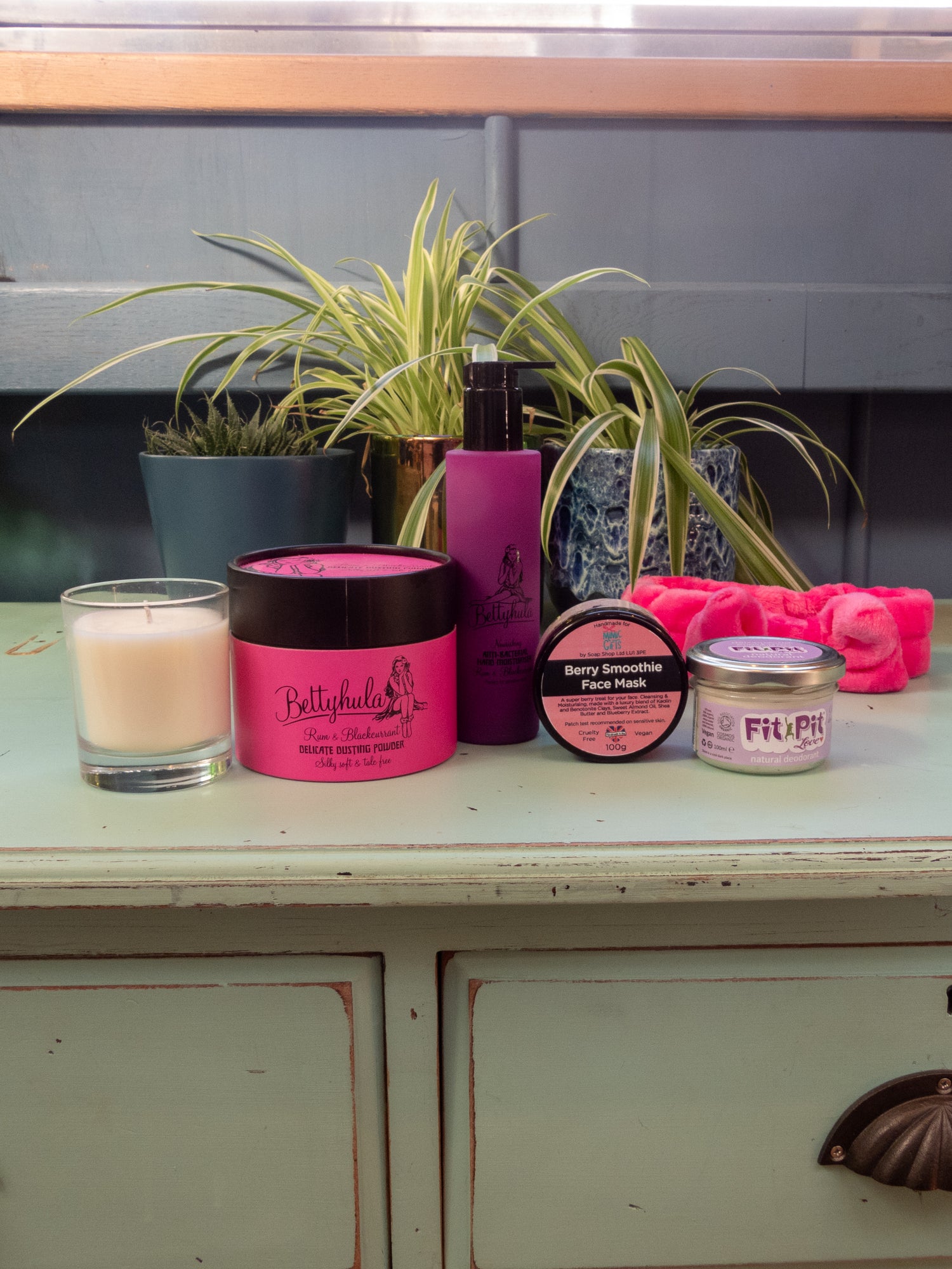 Vegan handcream, plastic-free talc, eco candle, kaolin clay facemask, hairband and fit pit deoderant displayed on a green dressing table