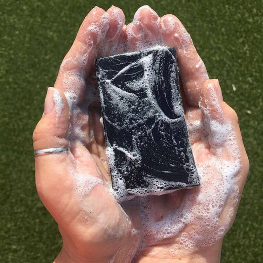 A bar Activated Charcoal handmade soap which is washing hands showing its gentle white lather