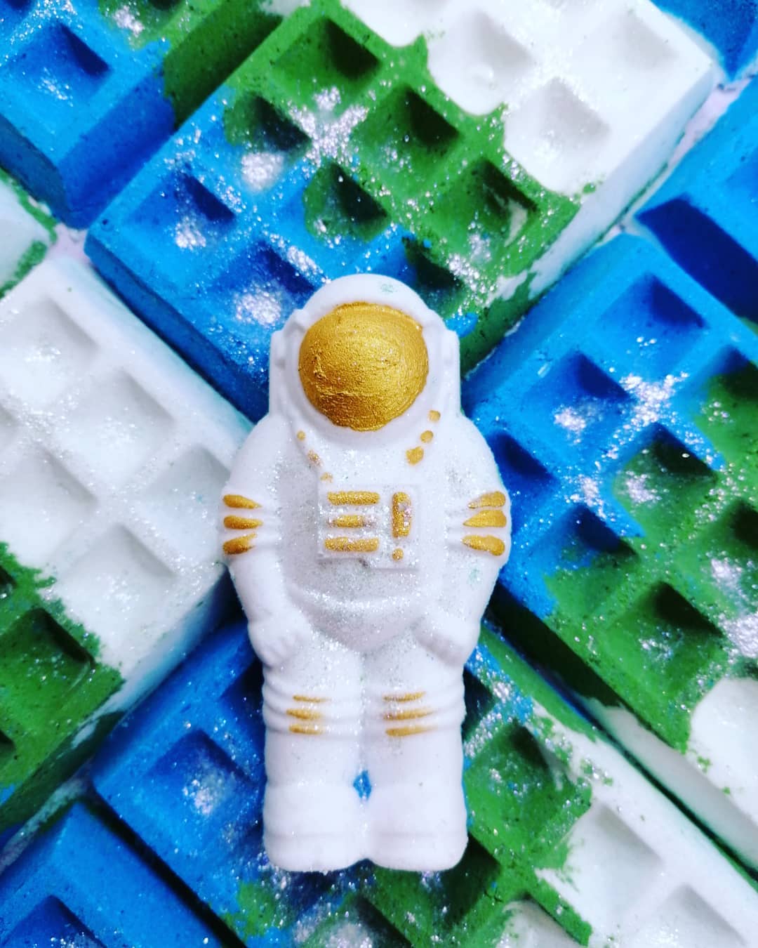 White & Gold vegan bath bomb in shape of a spaceman with its hidden colours of green & blue being shown in background