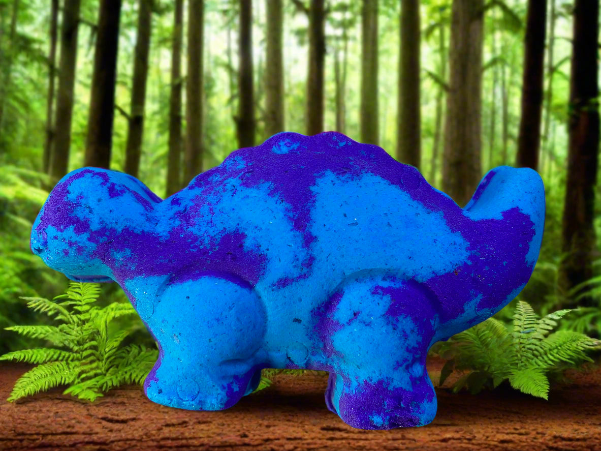 A bright blue Dinosaur Bath Bomb stands amoung green plants and tall trees