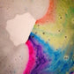 Cloud shaped vegan bath bomb fizzing in abath whilst emitting a rainbow of colours into the water