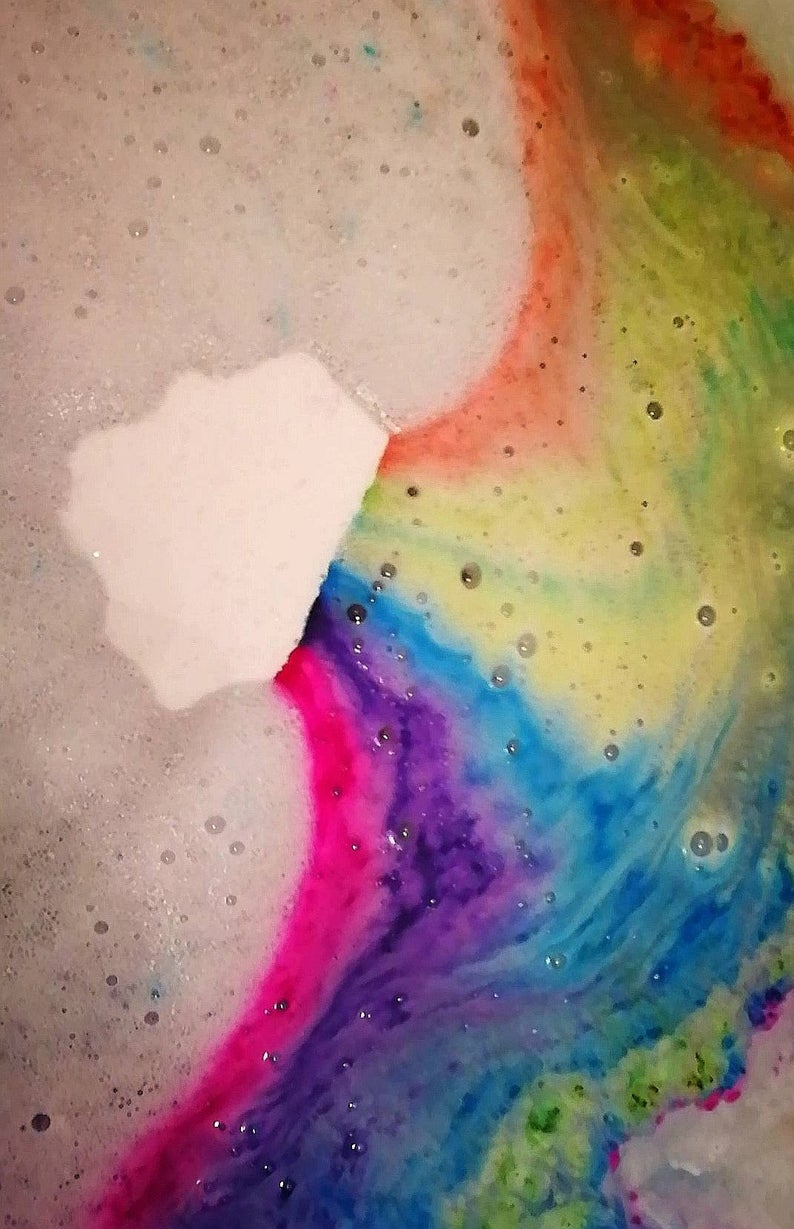 Cloud shaped vegan bath bomb fizzing in abath whilst emitting a rainbow of colours into the water