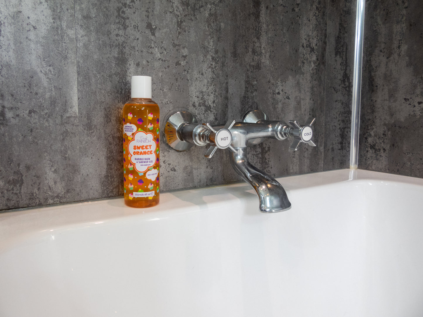 Bright orange sls-free & Vegan bubble bath shower gel bottle sitting on bath tub next to taps